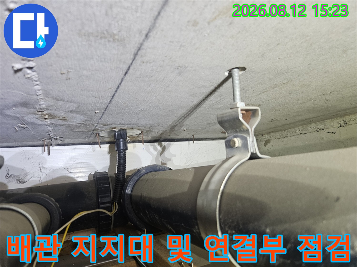 금속 행거로 고정된 검은색 천장 배관과 주변 콘크리트 구조물