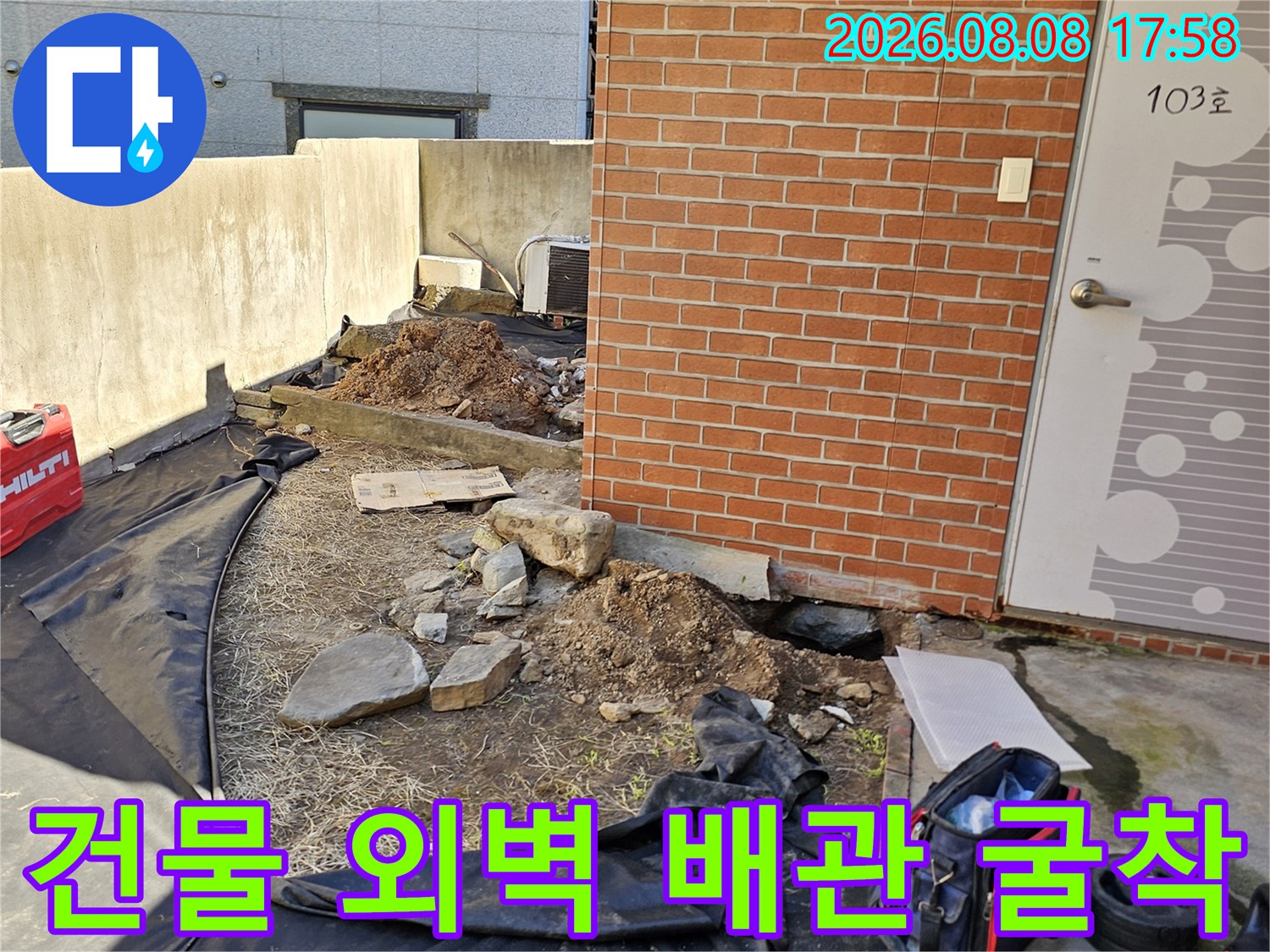 붉은 벽돌 건물 앞 - 누수 지점을 찾기 위해 바닥을 파헤친 작업 현장입니다.