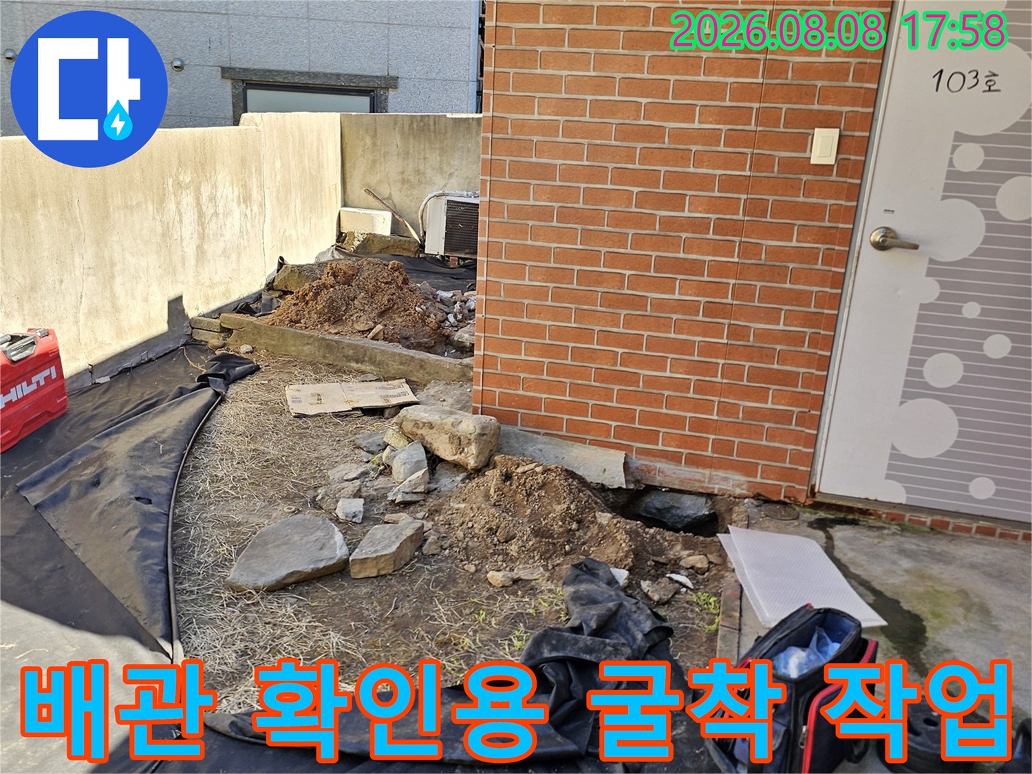 붉은 벽돌 건물 옆 - 누수 탐지를 위해 흙을 파낸 현장 모습