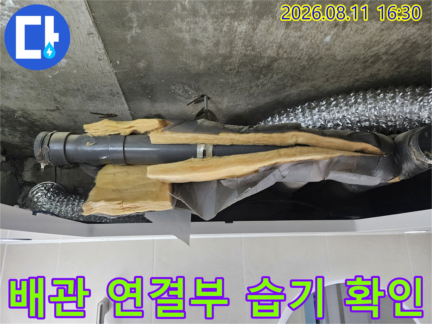 천장 내부의 은박 보온재로 감싸진 배관과 주변의 젖은 상태를 보여줍니다.