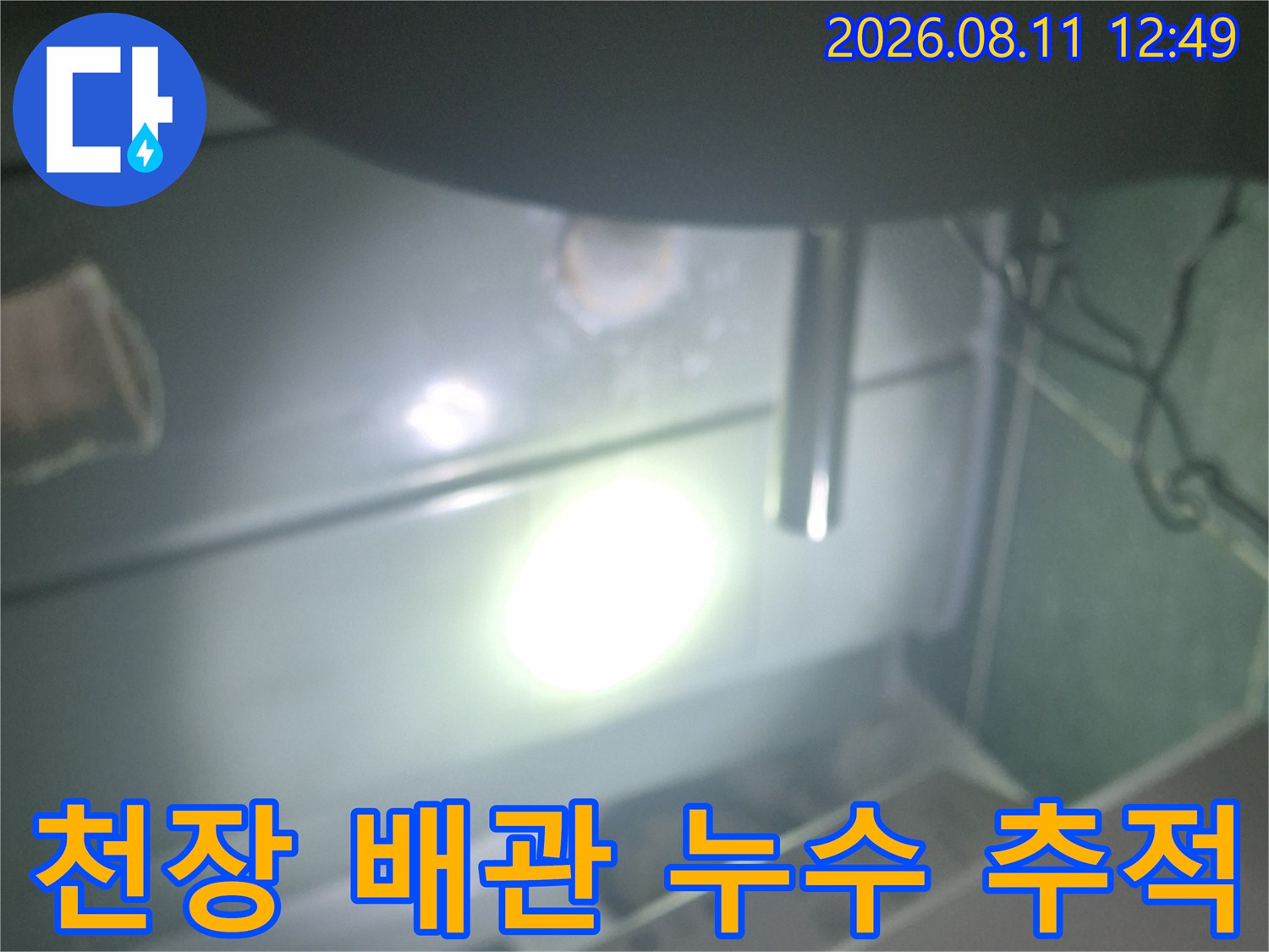손전등을 이용해 어두운 천장 안쪽의 배관 연결 부위를 자세히 살피고 있습니다.
