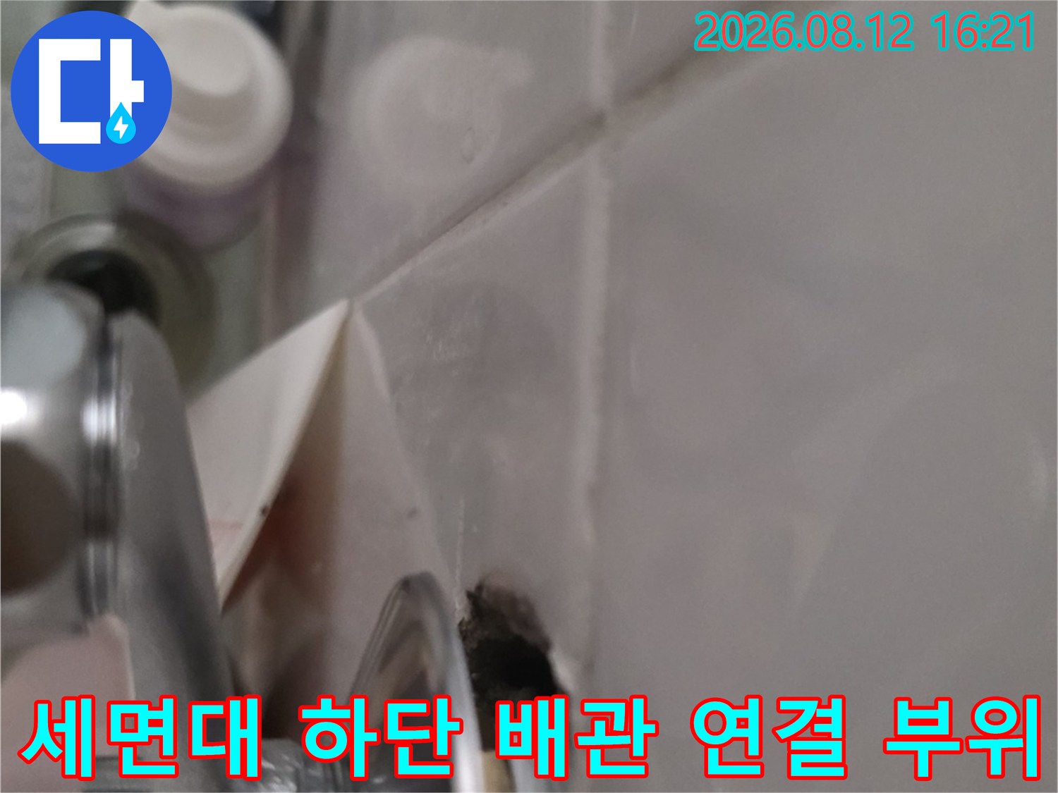 화장실 세면대 아래쪽의 금속제 배관 연결부와 천장 타일 접합 지점 사진