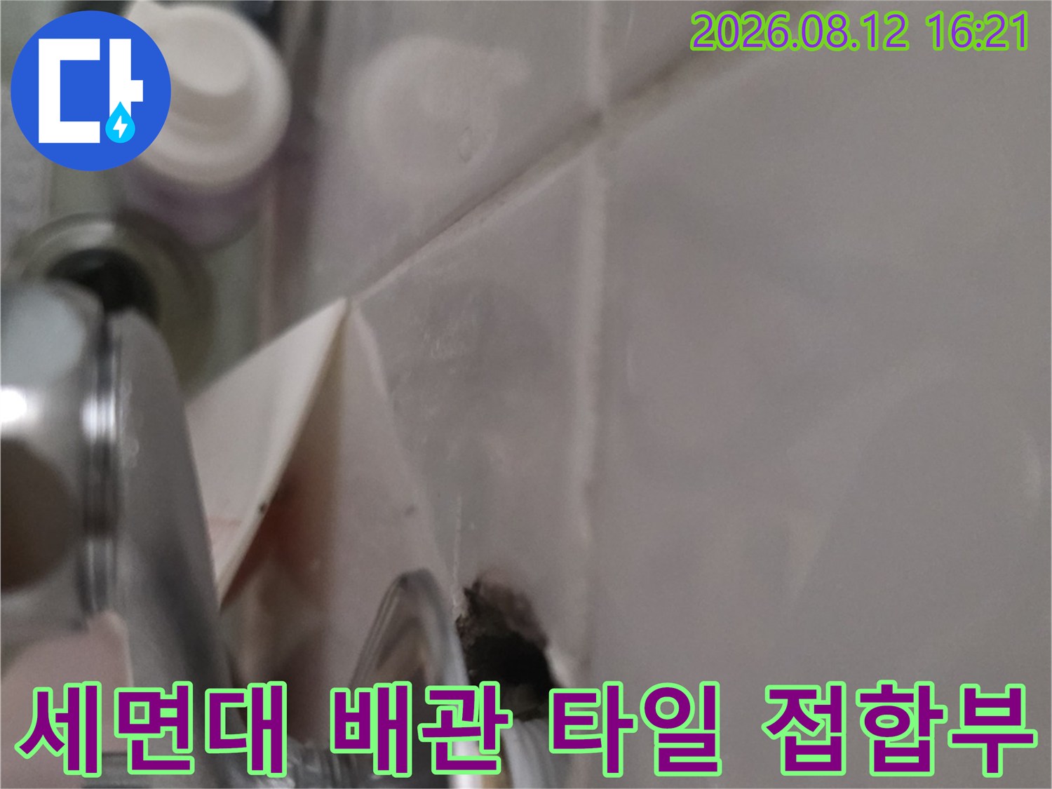 흰색 욕실 타일과 은색 금속-배관 연결부가 만나는 지점을 근접 촬영한 사진