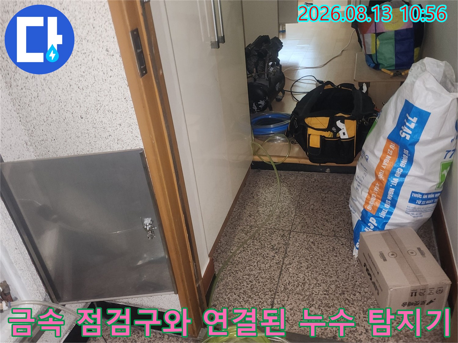 스테인리스 재질의 바닥 점검구 옆으로 노란색 호스가 배관에 연결되어 있는 사진