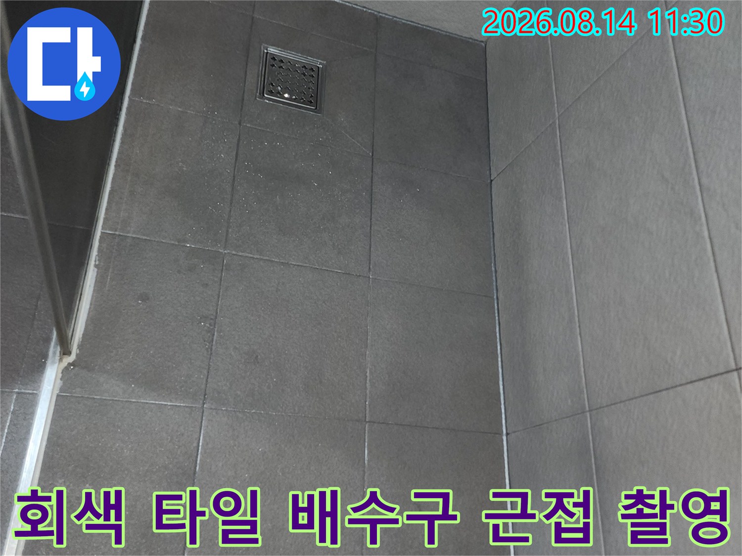 어두운 톤의 욕실 타일과 금속 재질의 배수구 유가 모습