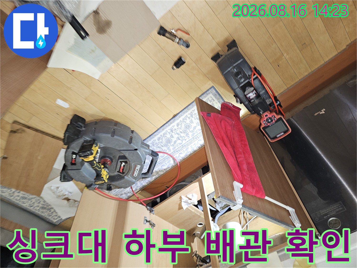 싱크대 아래 배관과 측정 장비가 배치된 작업 현장의 모습입니다.