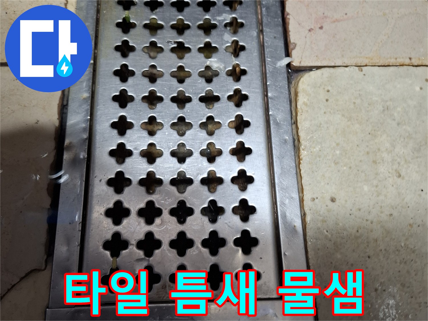 스테인리스 트렌치 주변의 갈라진 타일 틈새를 근접 촬영한 이미지입니다.