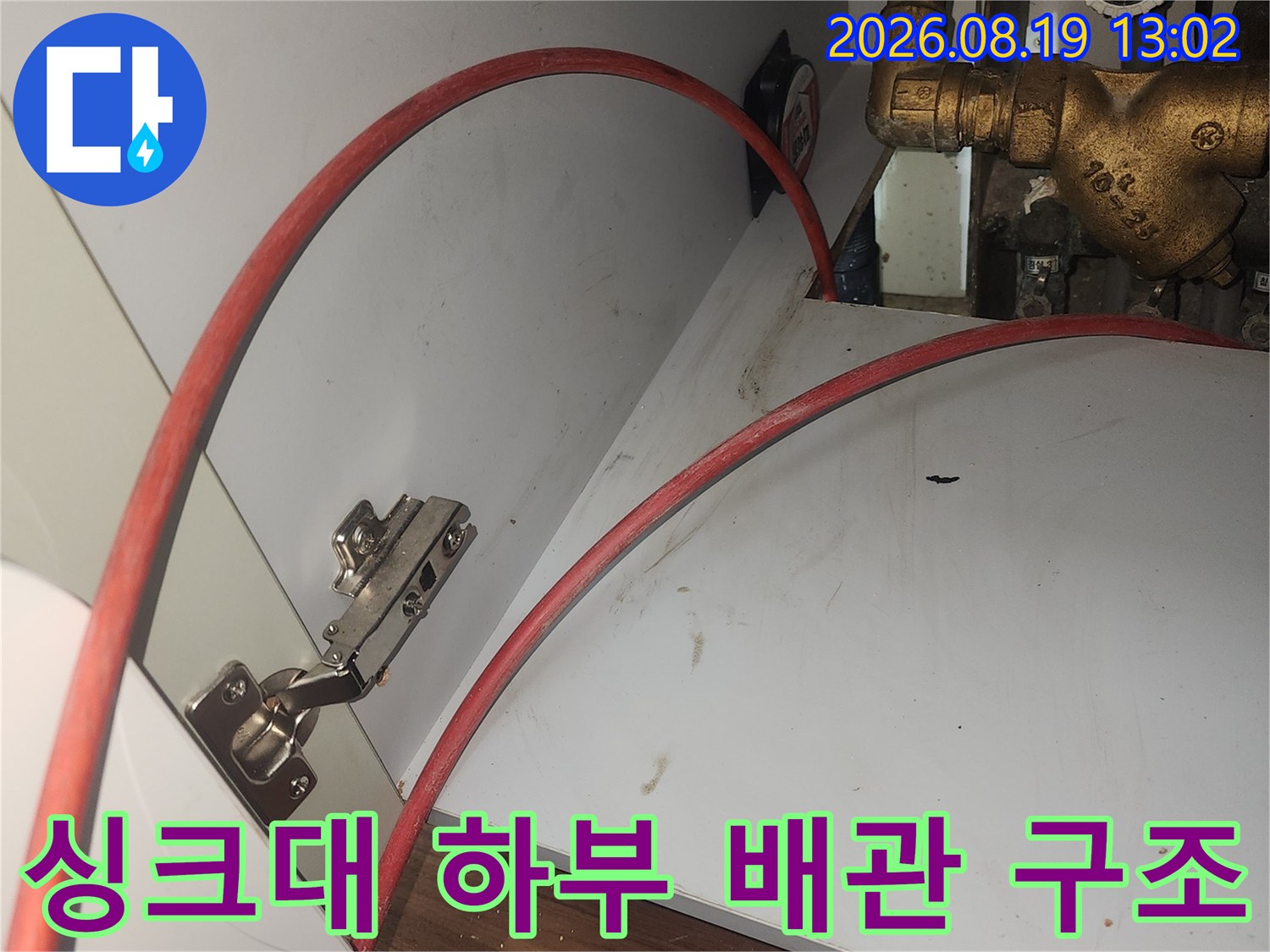 싱크대 하단 금속 배관과 붉은 호스가 연결된 모습