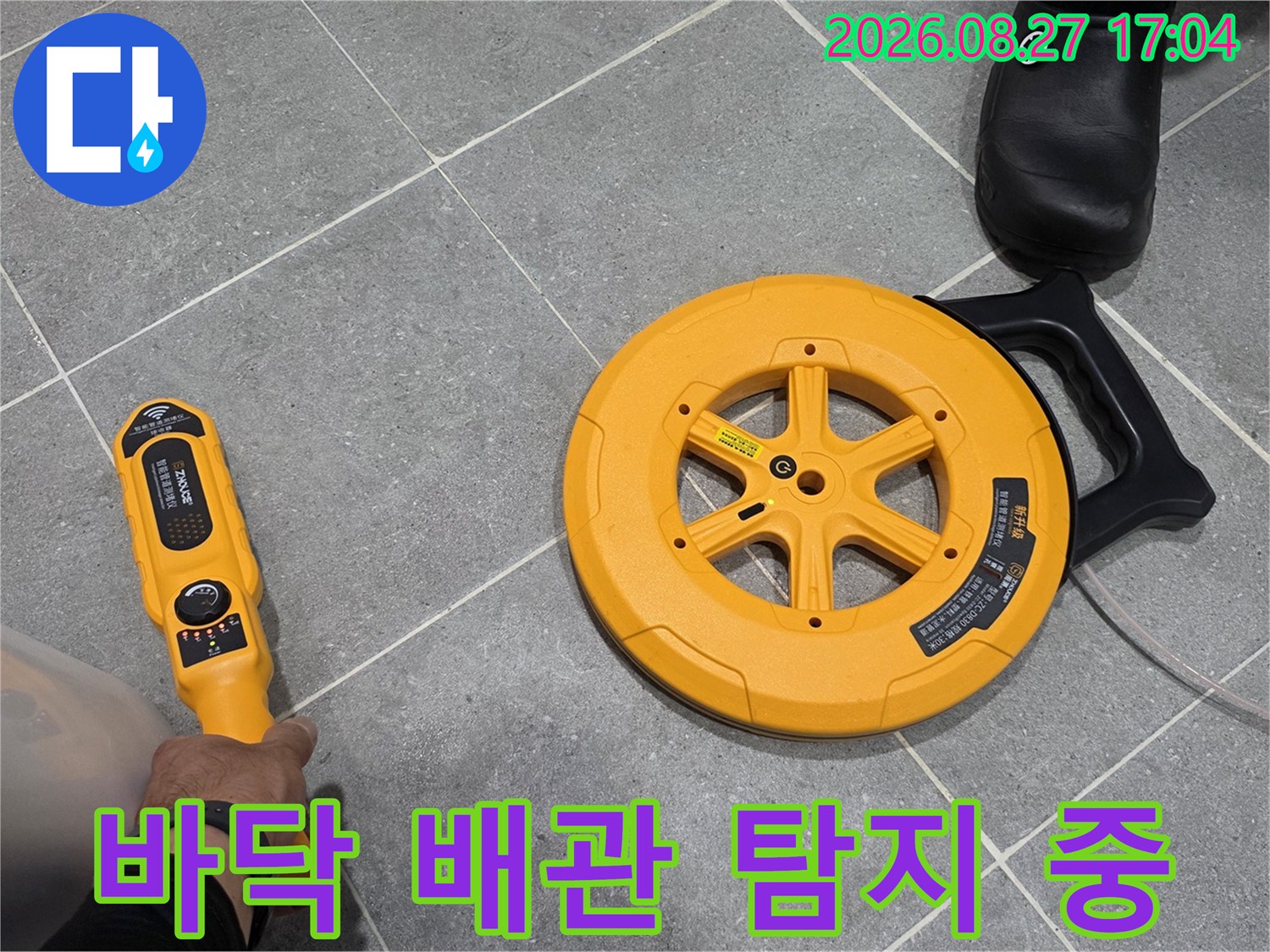 회색 욕실 타일 위에서-배관 탐지기를 조작하며 위치를 찾는 모습