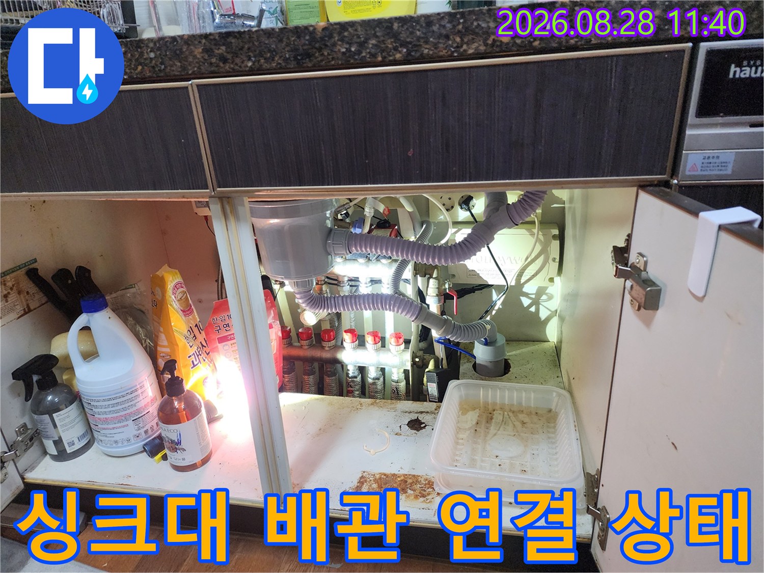 싱크대 하부장 내부에 배치된 굴곡진 호스와 여러 가지 배관 부속품들
