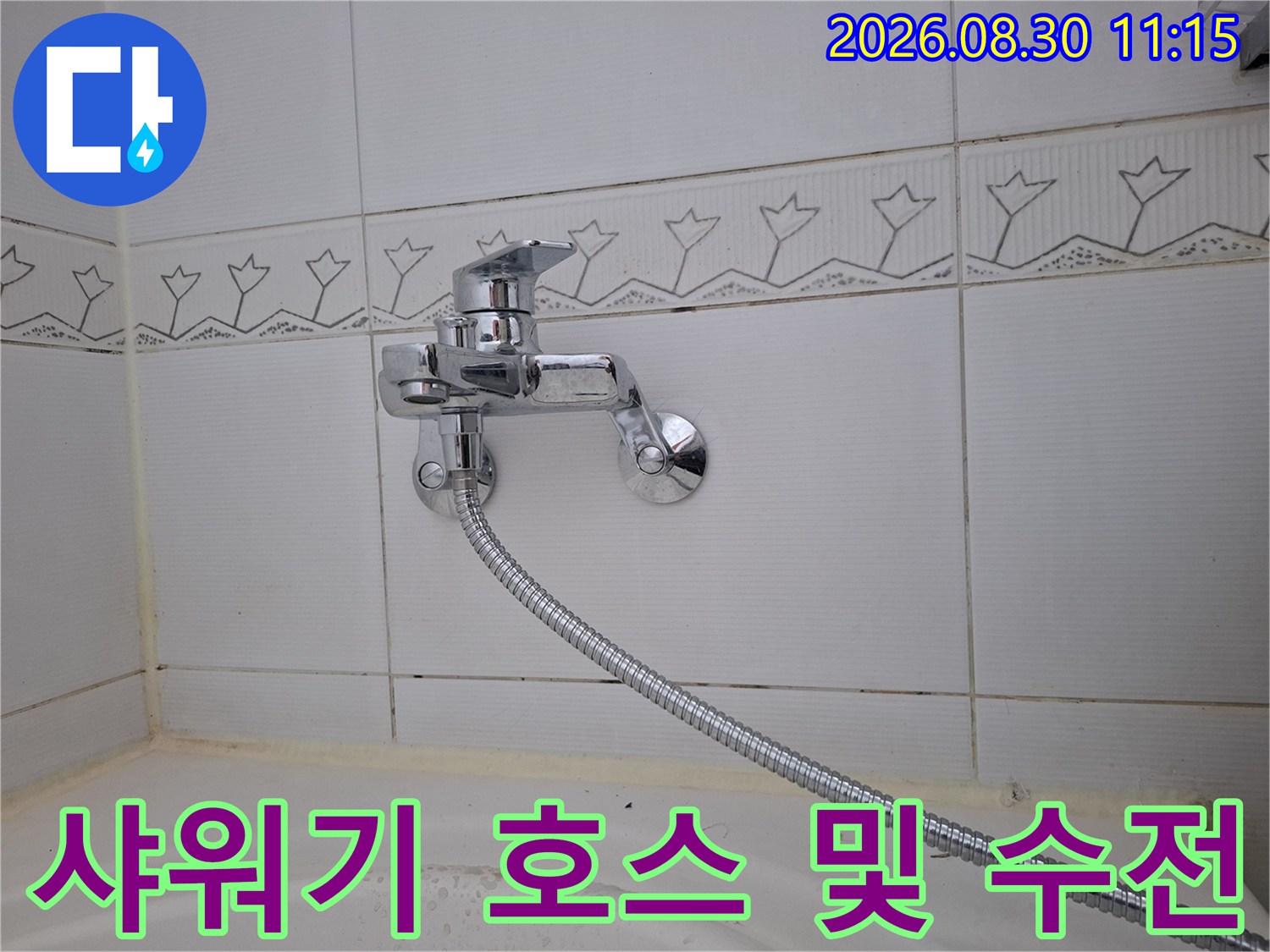 욕조 벽면 타일에 고정된 샤워 수전과 은색 호스 상세 샷