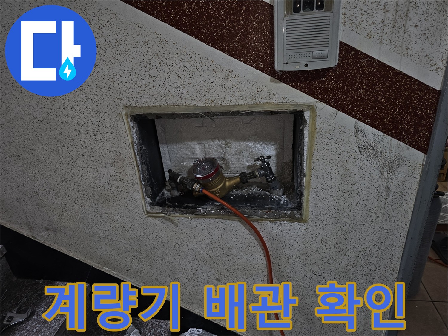 벽면 타공 부위 내부로 보이는 수도 계량기와 점검용 호스 연결 모습