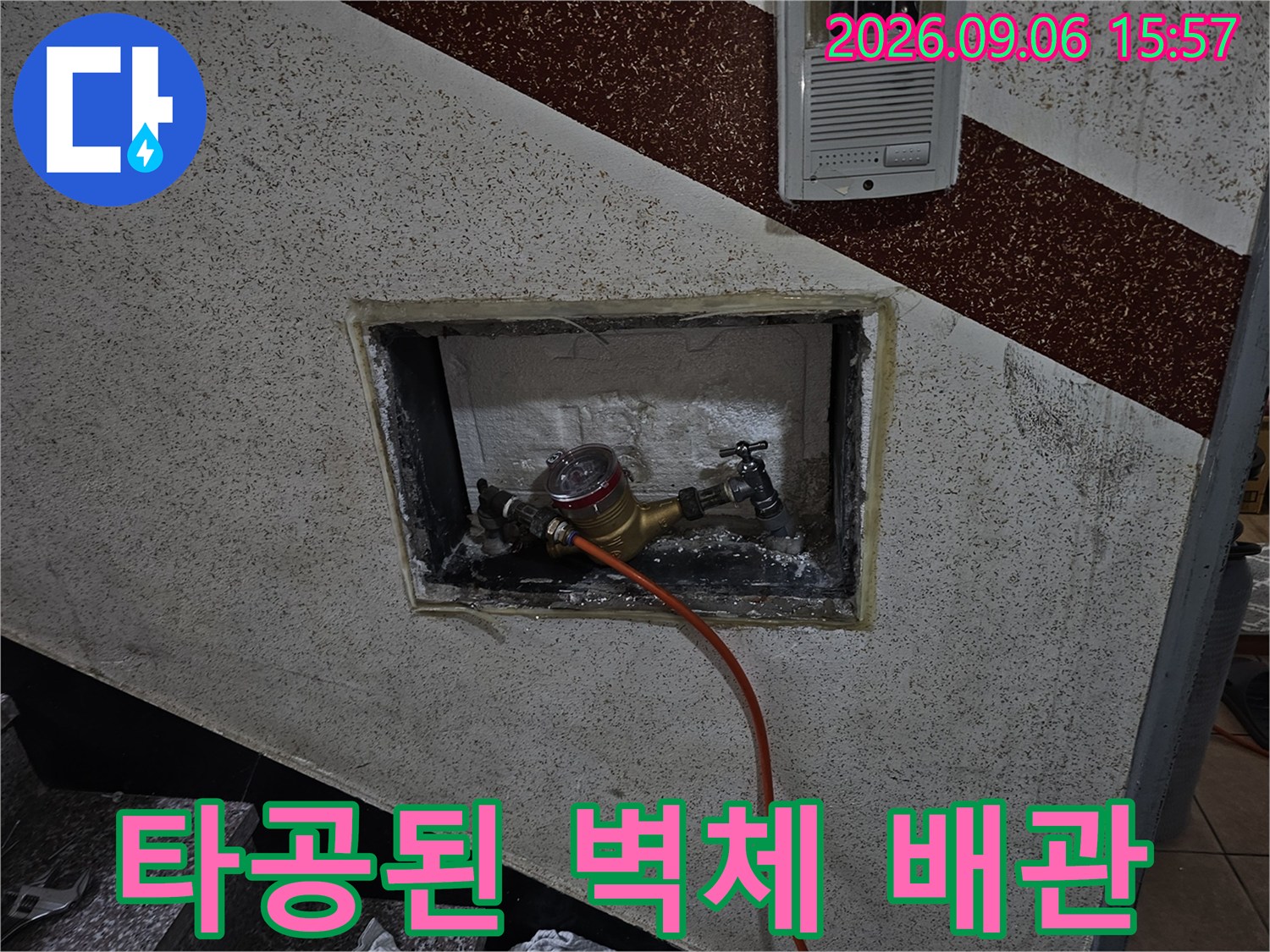 벽면 타공 부위 - 드러난 금속 배관과 점검용 주황색 호스 연결