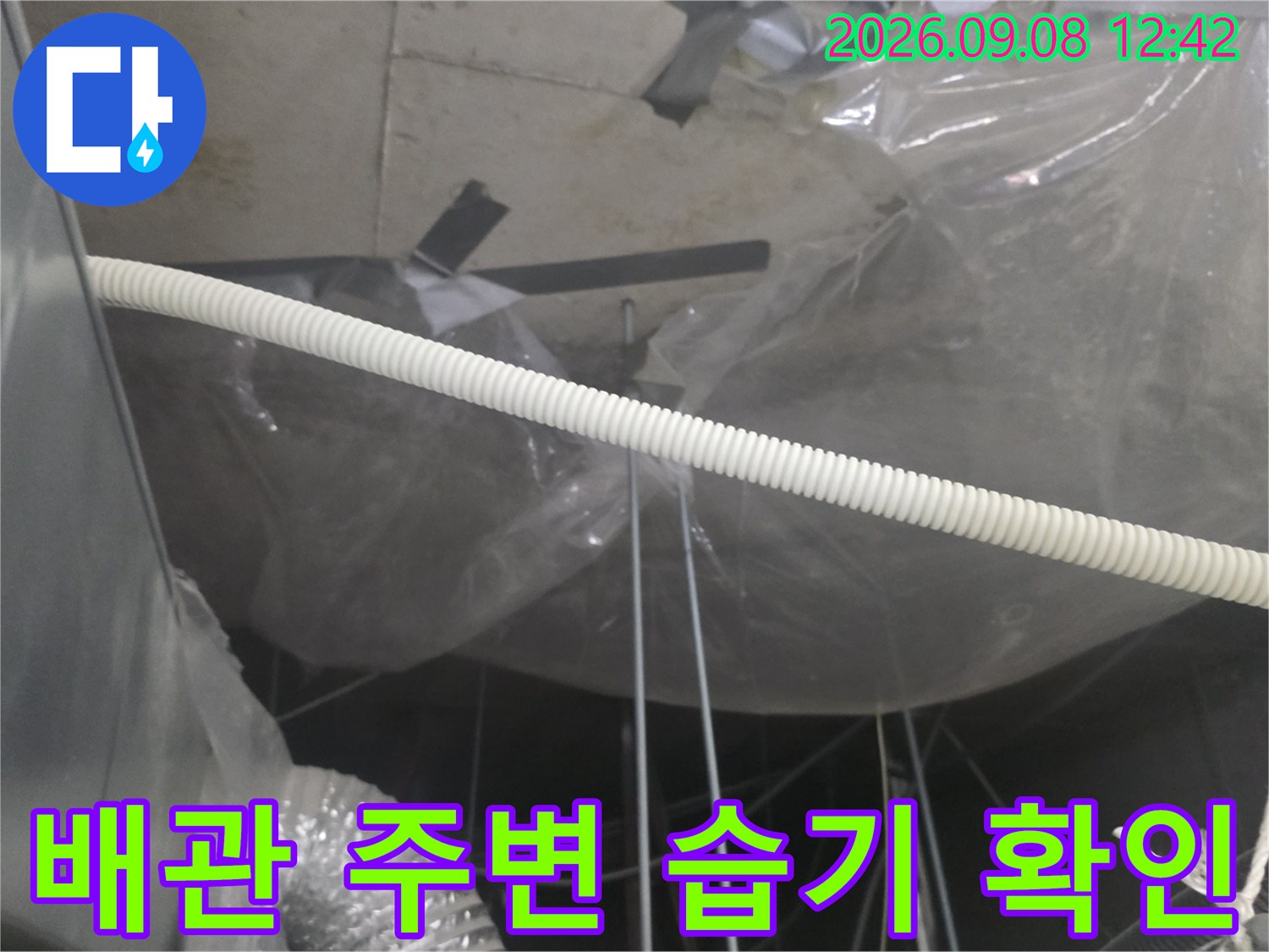 비닐 보양 처리된 천장 내부의 배관과 오염된 콘크리트 면을 보여줍니다.
