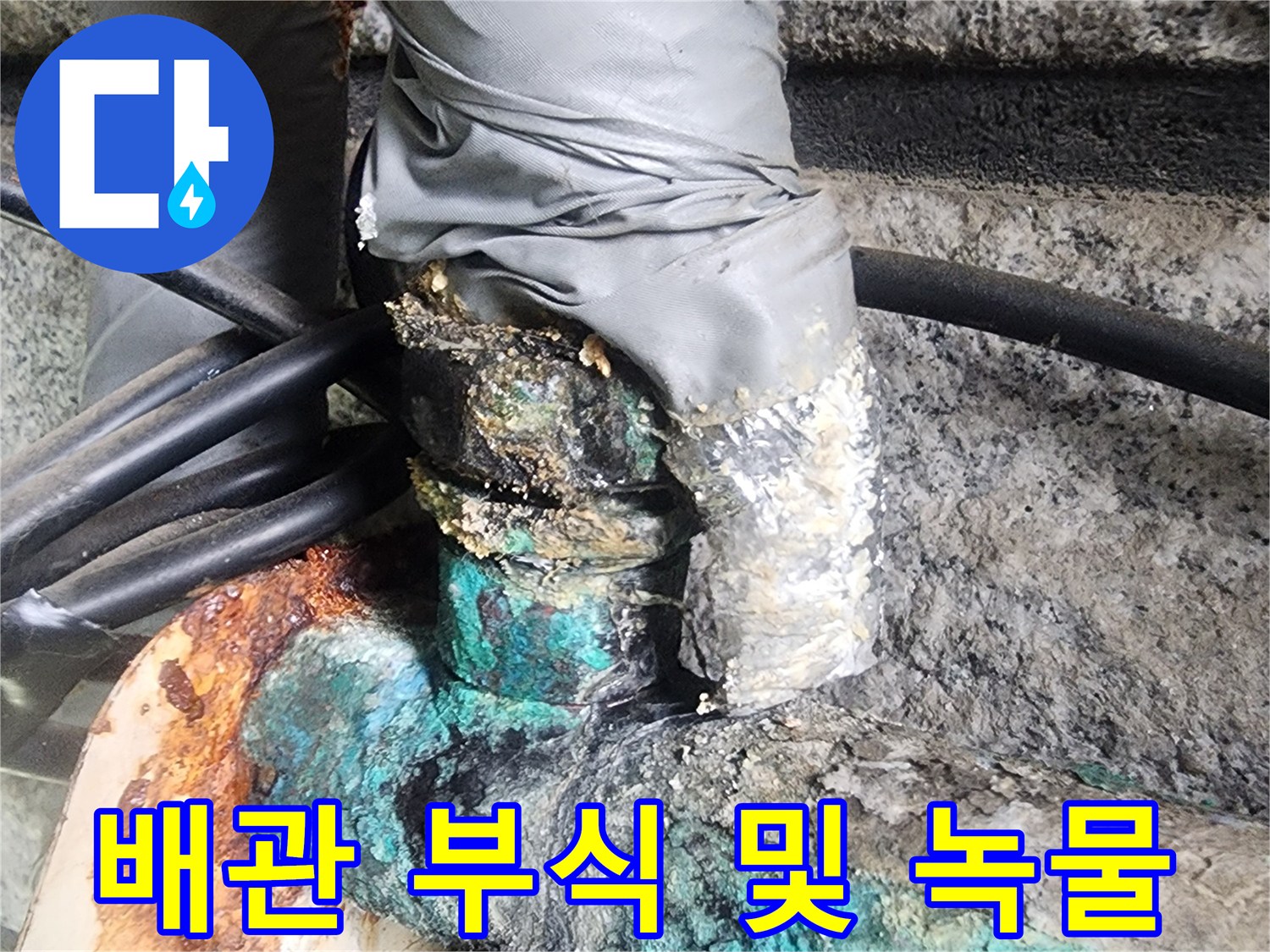 은색 마감재와 푸른 부식이 섞인 배관 연결부