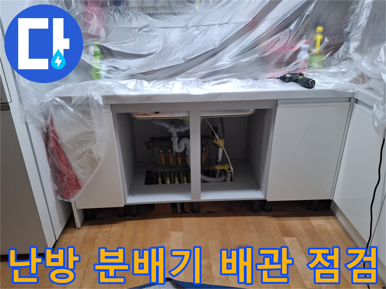 싱크대 하부장 내부에 노출된 난방 배관과 분배기 모습