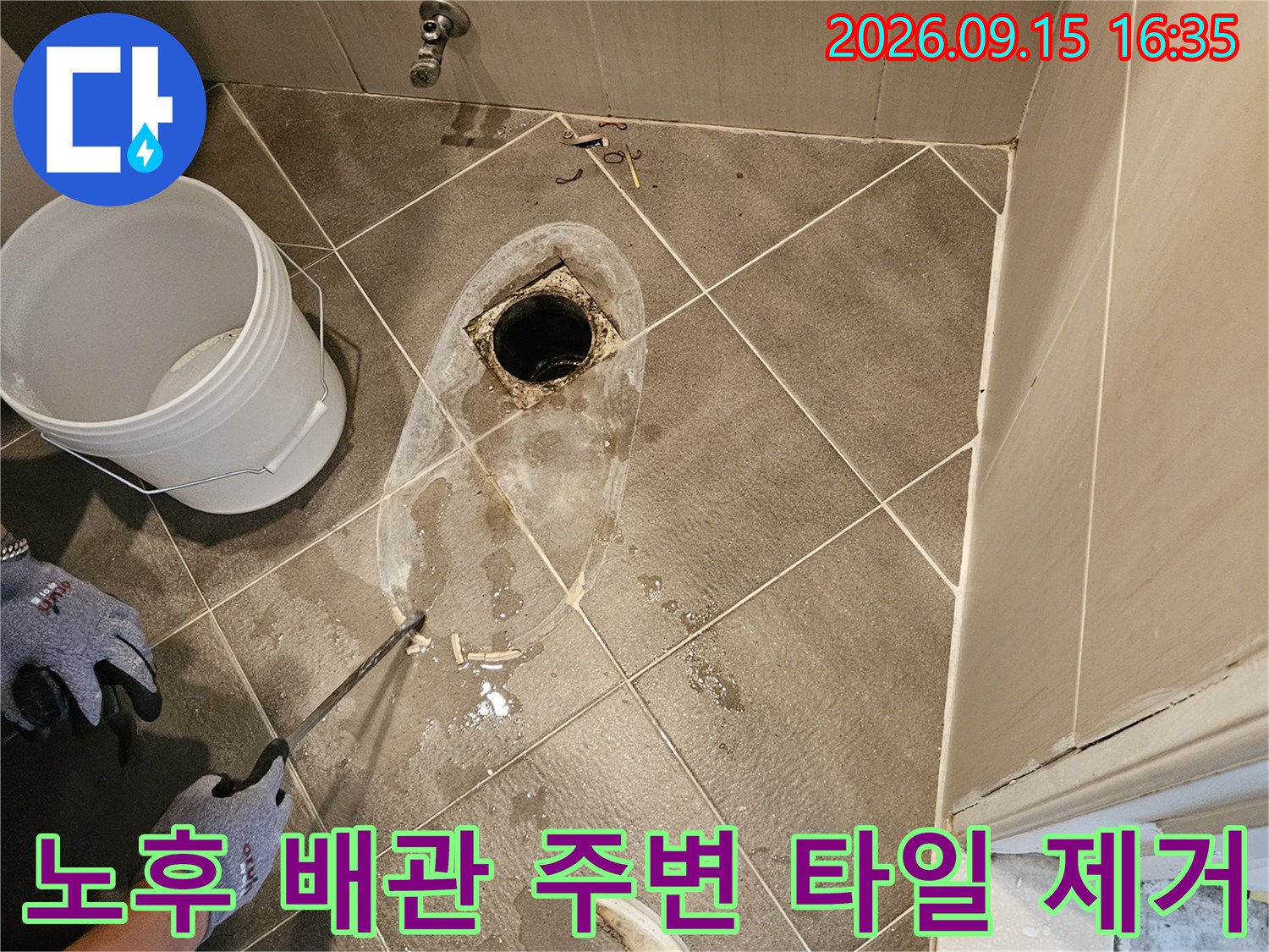노후된 배수구 배관 주변의 타일 조각들이 흩어져 있는 작업 현장 사진입니다.