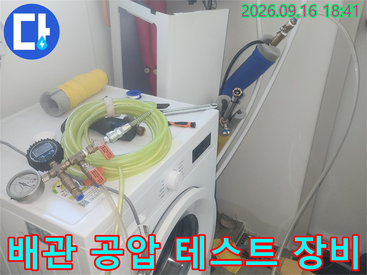 세탁실 수도 밸브에-연결된 압력계와 공압 검사용 호스들의 모습입니다.